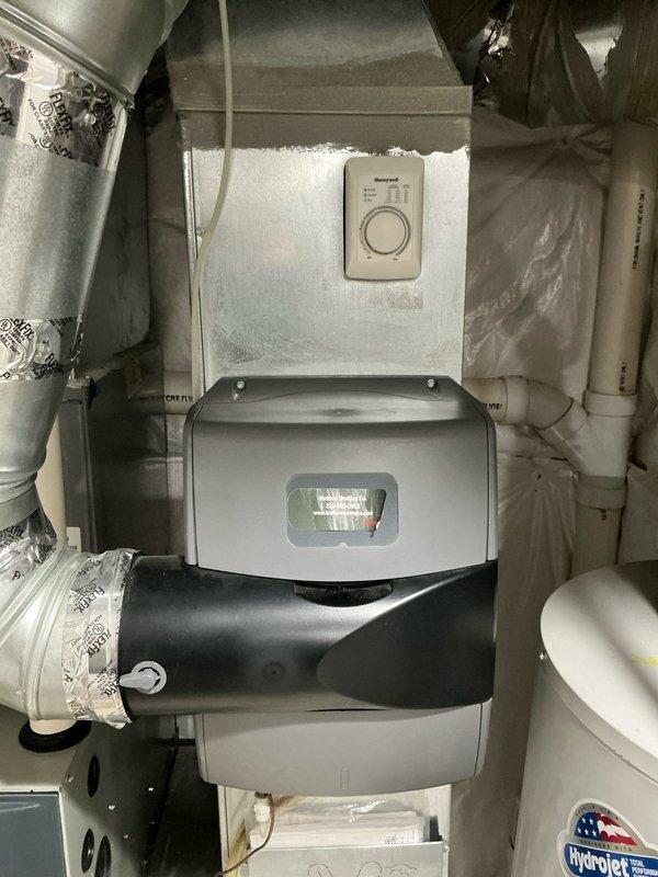 Conducted comprehensive assessment of existing residential HVAC system located in attic space for equipment replacement estimate. Evaluated current configuration including furnace, air handler, humidification system, and associated ductwork components. Documented existing installation featuring stacked unit assembly with thermostat control, gray housing unit, black cylindrical humidifier with connection ports, and HydroJet equipment. Photographed copper refrigerant lines, condensate drainage system with PVC piping, and electrical connections mounted to metal ductwork panel. Provided customer with multiple replacement options alongside available repair alternatives for consideration.