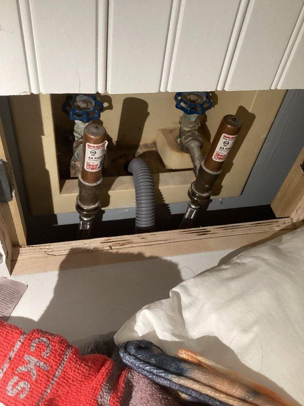 Responded to plumbing inspection request for reported valve leak. Upon arrival, accessed ceiling cavity to inspect water shut-off valves and associated piping. Identified water staining and discoloration on ceiling surface near center valve assembly, indicating active or recent leak from shut-off valve connection. Documented existing conditions with photographs showing two water shut-off valves with blue handles mounted to underside of floor structure, with visible moisture damage patterns. 

Proceeded to basement utility area to inspect related plumbing system components. Examined black circulation pump unit with multiple copper pipe connections, brass valves, and PVC discharge piping. Verified proper operation of pump assembly and checked all soldered copper joints and threaded connections for signs of seepage or moisture. Inspected white PVC discharge line with elbow joint secured by metal hose clamps for proper installation and secure mounting.

Confirmed leak source at upper valve