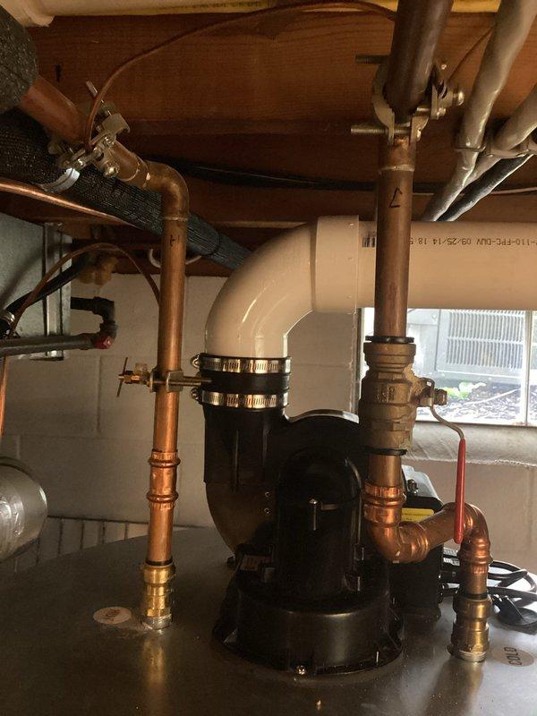 Responded to plumbing inspection request for reported valve leak. Upon arrival, accessed ceiling cavity to inspect water shut-off valves and associated piping. Identified water staining and discoloration on ceiling surface near center valve assembly, indicating active or recent leak from shut-off valve connection. Documented existing conditions with photographs showing two water shut-off valves with blue handles mounted to underside of floor structure, with visible moisture damage patterns. 

Proceeded to basement utility area to inspect related plumbing system components. Examined black circulation pump unit with multiple copper pipe connections, brass valves, and PVC discharge piping. Verified proper operation of pump assembly and checked all soldered copper joints and threaded connections for signs of seepage or moisture. Inspected white PVC discharge line with elbow joint secured by metal hose clamps for proper installation and secure mounting.

Confirmed leak source at upper valve