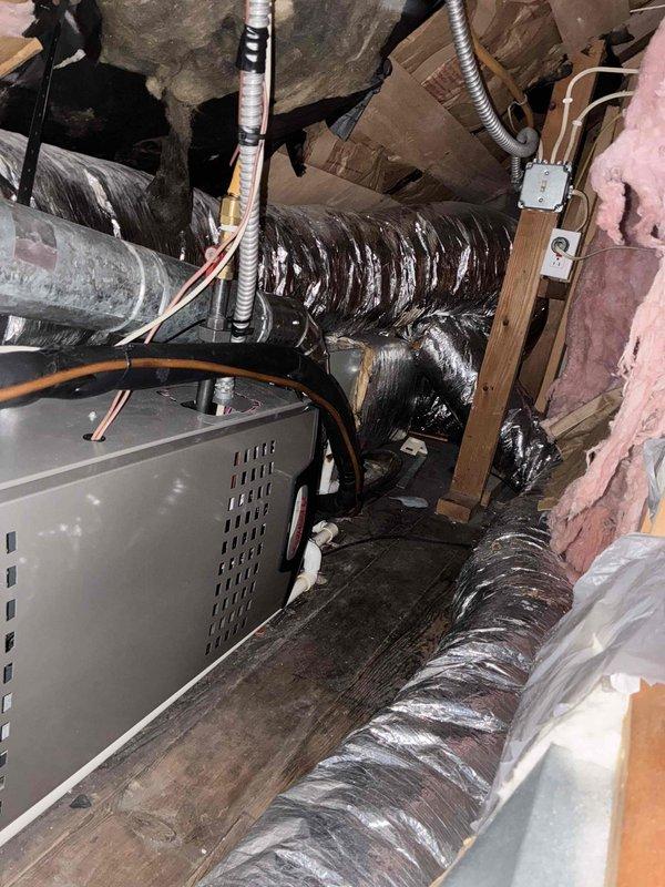 Conducted comprehensive attic inspection and assessment for full HVAC system replacement estimate at residential property. Evaluated existing air handler unit #152 and associated ductwork, noting cramped attic installation with flexible black ductwork, copper refrigerant lines, and pink fiberglass insulation throughout confined space. Documented significant moisture damage and black staining with white streaking patterns on roof decking above equipment, indicating potential mold growth or water intrusion requiring remediation. Assessed condition of gray metal HVAC equipment with visible copper lines and flexible metal ductwork secured with foil tape at connections. Provided estimate options for replacement of at least one air conditioning unit with consideration for complete system replacement plus additional AC unit installation to meet customer requirements.