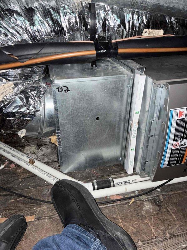 Conducted comprehensive attic inspection and assessment for full HVAC system replacement estimate at residential property. Evaluated existing air handler unit #152 and associated ductwork, noting cramped attic installation with flexible black ductwork, copper refrigerant lines, and pink fiberglass insulation throughout confined space. Documented significant moisture damage and black staining with white streaking patterns on roof decking above equipment, indicating potential mold growth or water intrusion requiring remediation. Assessed condition of gray metal HVAC equipment with visible copper lines and flexible metal ductwork secured with foil tape at connections. Provided estimate options for replacement of at least one air conditioning unit with consideration for complete system replacement plus additional AC unit installation to meet customer requirements.