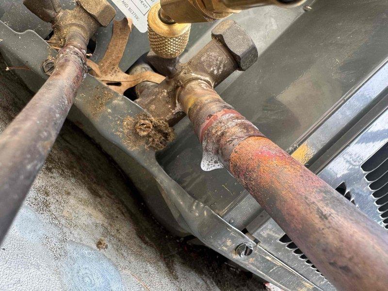 Performed leak search on HVAC system using digital micron gauge to diagnose refrigerant loss. Located significant corrosion on refrigerant piping and fittings, with heavy rust buildup on connection points indicating the source of the leak. Documented system condition showing deteriorated copper lines and corroded service ports requiring attention to restore proper system operation.