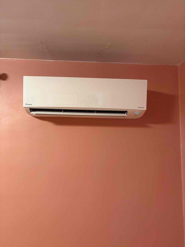 Completed installation of Daikin ductless mini-split system consisting of one indoor wall-mounted air handler unit and one outdoor condenser unit. The outdoor unit was positioned on a concrete pad in the yard area, with refrigerant lines and electrical connections properly routed to the interior air handler mounted on the wall, ensuring efficient operation of the single-head mini-split system.