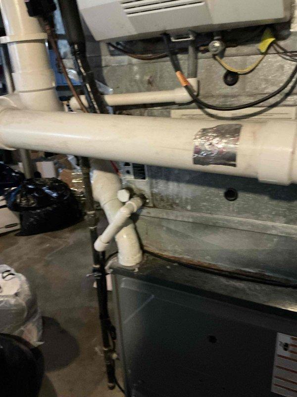 Documented existing HVAC system configuration in basement mechanical room, including Aprilaire humidifier unit with associated PVC plumbing and electrical connections. Photographed current equipment installation showing white PVC piping with metallic tape repair section, concrete block wall mounting, and ductwork connections to provide comprehensive visual reference for replacement system specifications and equipment upgrade options.