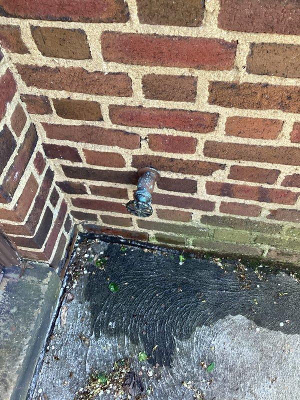 Responded to customer complaint of low water pressure affecting multiple faucets throughout the home. Upon investigation, discovered significant corrosion and mineral buildup in the main water supply lines located in the basement utility area. Identified rust-colored staining and oxidation on metal pipes and fittings, indicating advanced deterioration of the plumbing system. Documented corroded piping with visible scale accumulation and discolored water present in collection bucket, confirming sediment contamination in the water supply. Assessed blue-handled ball valve and surrounding pipe connections showing signs of aging and potential flow restriction. Exterior inspection revealed moisture intrusion at foundation level with algae growth on brick surfaces, suggesting possible water supply line issues contributing to pressure problems. Photographed affected areas for documentation and recommended comprehensive evaluation of water supply system to address corrosion-related flow restric