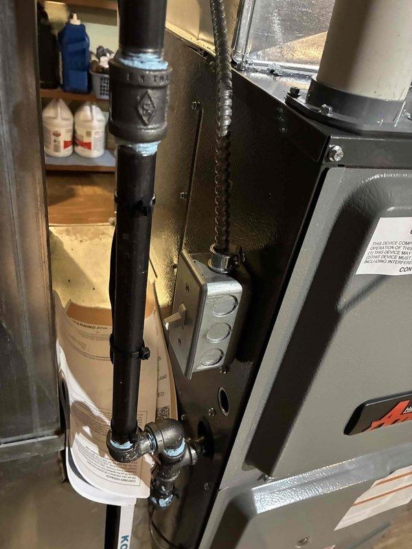 Completed installation of new Amana 96% AFUE high-efficiency gas furnace in basement utility area. System includes PVC venting routed through existing ductwork connections, gas piping with black iron threaded fittings, and unit mounted on concrete pad with proper clearances maintained. All connections tested and operational, with furnace commissioned and verified for proper heating cycle operation.