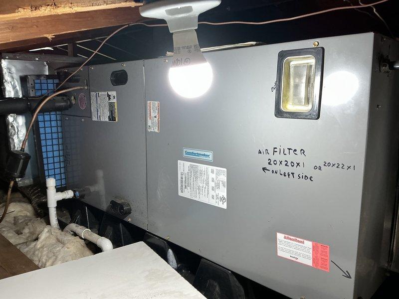 Conducted comprehensive evaluation of existing HVAC system for replacement estimate. Documented outdoor condensing unit positioned against exterior wall with refrigerant lines running along ground through landscaping area. Assessed indoor air handler unit installed in attic space, noting ComfortMaker equipment with accessible filter location marked on cabinet. Photographed both components to provide visual documentation of current system configuration, equipment condition, and installation environment for replacement options analysis.