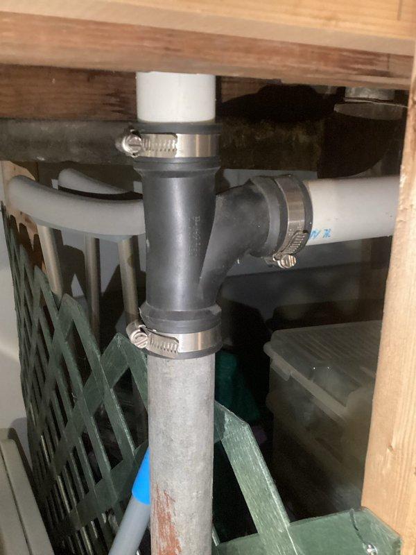 Provided plumbing estimate for replacing flexible drain assemblies with solid PVC drain lines and P-traps in three bathroom locations: master bath, first floor bath, and second floor bath. Estimate included sealing an access hole in the second floor bathroom using expanding foam insulation, and replacing a wye drain fitting under the stairs with solid pipe configuration. Documented existing plumbing conditions showing current flexible drain connections and PVC drainage assemblies secured with hose clamps.