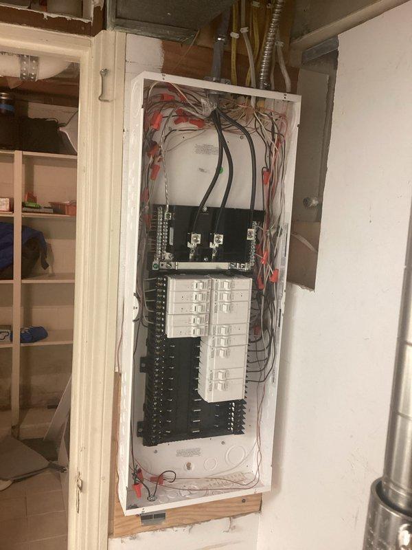 # Partial Rewire - 200 Amp Service Upgrade

Completed a comprehensive partial rewire with 200 amp service upgrade involving replacement and installation of two electrical panels. The interior panel was surface-mounted on wooden backing in the basement utility area, featuring dual circuit breaker arrays with proper color-coded wiring (red, black, white) connected to main bus bars. Three large main power feed cables were terminated at the top of the panel with appropriate connectors.

The exterior panel was mounted on the building's vinyl siding and included a main disconnect switch at the top with dual feed cables entering through the enclosure. Below the disconnect, installed a full complement of circuit breakers arranged in standard residential configuration. Multiple branch circuits were connected using properly sized conductors in various colors including red, black, white, yellow, and green wiring. Gray PVC conduit entries were installed at the bottom of the exterior panel for prot