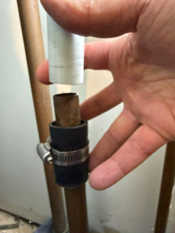 Responded to service call for water leakage at condensate drain connection on recently installed furnace system. Upon inspection, identified improper connection between new condensate pipe and existing drainage pipe secured with rubber sleeve coupling and hose clamp, which had failed and was causing water to leak onto the floor. Documented the faulty connection point showing deteriorated coupling between white PVC condensate line and existing tan drainage pipe. Repaired or replaced the defective rubber coupling to restore proper drainage and prevent further water damage.