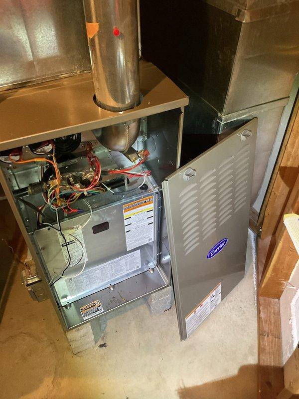Performed comprehensive preventive maintenance on residential Carrier HVAC cooling system. Inspected internal components including refrigerant lines, electrical connections, and burner assembly with all systems found to be operating within normal parameters. Documented equipment condition through photographic records showing furnace unit with exposed mechanical components and ductwork in basement installation.