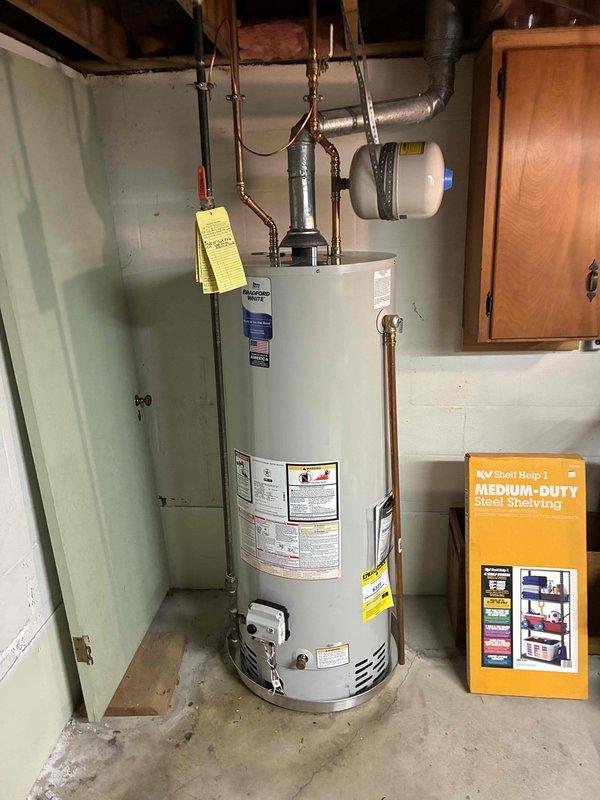 Replaced 40-gallon residential water heater in basement utility room. Installed new white cylindrical water heater with proper copper piping connections, expansion tank, and safety valves. Connected unit to existing plumbing infrastructure with appropriate fittings and secured all overhead components. Removed and placed old tank outside per customer instructions. All connections tested and verified operational.