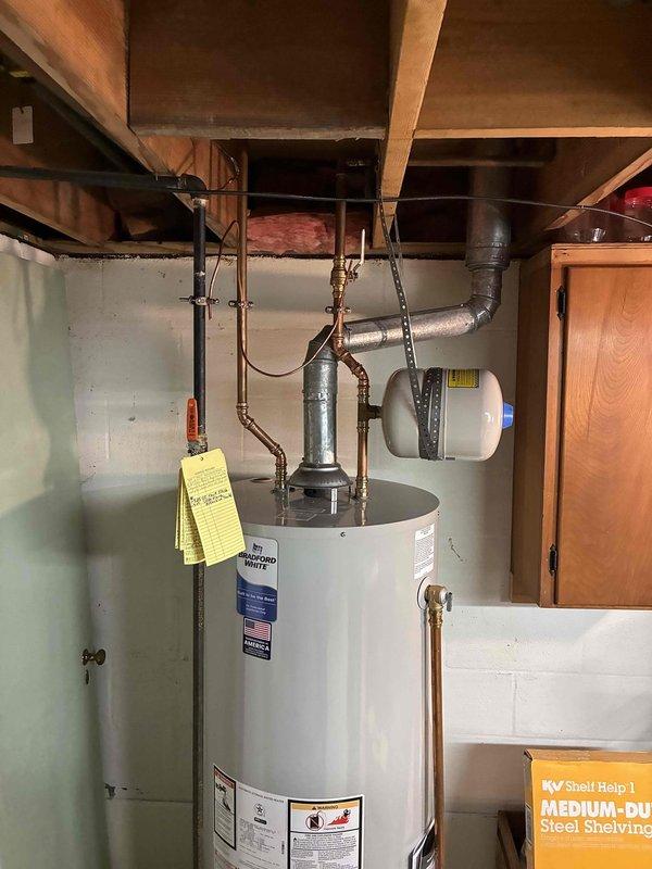Replaced 40-gallon residential water heater in basement utility room. Installed new white cylindrical water heater with proper copper piping connections, expansion tank, and safety valves. Connected unit to existing plumbing infrastructure with appropriate fittings and secured all overhead components. Removed and placed old tank outside per customer instructions. All connections tested and verified operational.