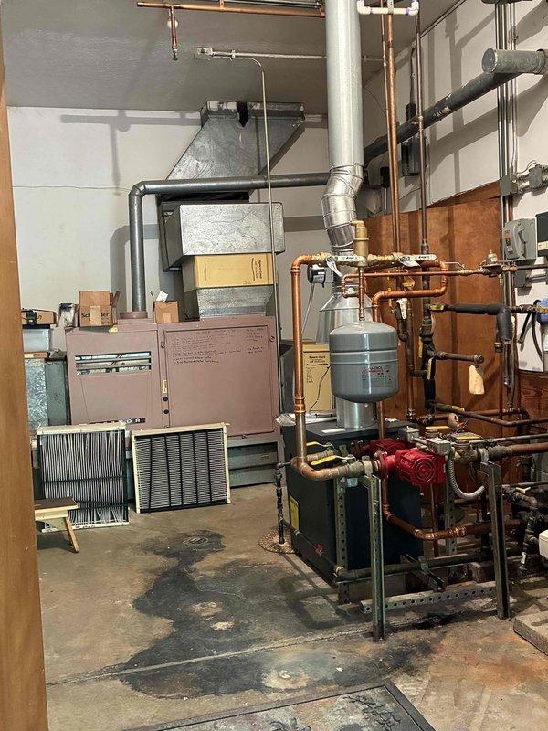 Responded to service call regarding air conditioning system that customer reported as non-operational following recent boiler installation in shared mechanical room. Upon inspection, verified that AC system had been inadvertently disconnected during previous boiler work three months prior. Documented existing conditions of mechanical room showing boiler installation, hydronic piping assembly with expansion tank, and air conditioning equipment. Photographed condensate drain pan showing signs of aging and oxidation, indicating system had not been operational for extended period.
