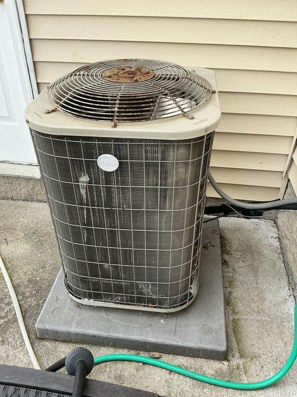 Responded to no cooling complaint on residential air conditioning system. Upon arrival, performed visual inspection of outdoor condenser unit, which showed signs of age with rust and corrosion visible on fan guard and general weathering of exterior components. Unit appeared to be installed on concrete pad with proper clearances maintained. Documented equipment condition through photographs showing cylindrical condenser with mesh grille housing and top-mounted fan assembly. Refrigerant lines observed running from unit to structure. Previous technician had visited property two days prior. System required diagnostic evaluation to determine root cause of cooling failure and restore proper operation.