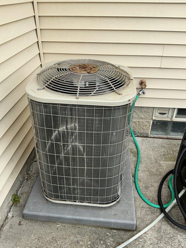 Responded to no cooling complaint on residential air conditioning system. Upon arrival, performed visual inspection of outdoor condenser unit, which showed signs of age with rust and corrosion visible on fan guard and general weathering of exterior components. Unit appeared to be installed on concrete pad with proper clearances maintained. Documented equipment condition through photographs showing cylindrical condenser with mesh grille housing and top-mounted fan assembly. Refrigerant lines observed running from unit to structure. Previous technician had visited property two days prior. System required diagnostic evaluation to determine root cause of cooling failure and restore proper operation.