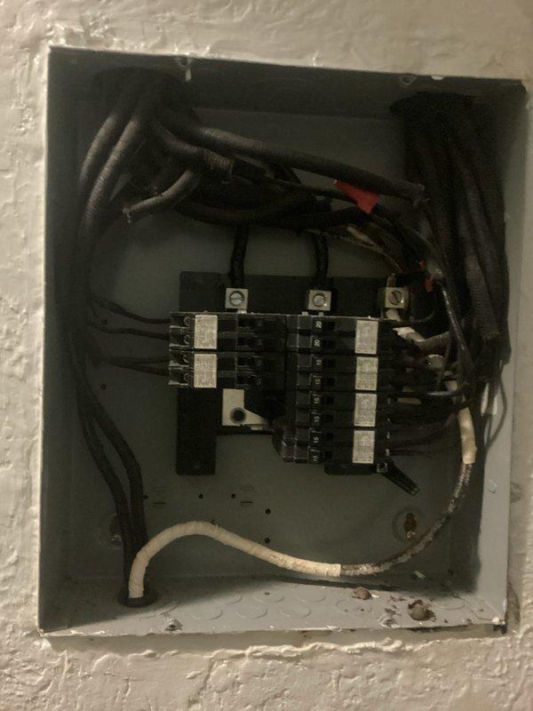 Conducted comprehensive electrical inspection of residential service panel and utility area. Documented existing panel configuration showing multiple circuit breakers with mixed wiring conditions, including visible age-related wear on enclosure and dust accumulation. Photographed utility connections and storage area layout for reference. Inspection revealed older electrical distribution system with exposed wiring bundles entering panel from multiple entry points and ground conductor properly terminated at panel base.