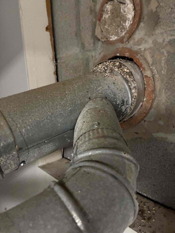 Responded to no cooling call on original 1980s HVAC system that trips breaker when switched from heat to cool mode. Upon inspection, found evaporator coil heavily clogged with dust and debris, restricting airflow significantly. Documented existing ductwork penetrations through foundation wall showing age-related deterioration and rust around collars. Identified copper refrigerant lines and coil housing with substantial dust accumulation throughout system. Explained that the breaker tripping is likely due to compressor overload caused by restricted airflow from the severely fouled evaporator coil, combined with age-related component failure in the outdoor condensing unit. Given the system's age of 40+ years and extent of deterioration, recommended full system replacement rather than repair. Customer expressed strong interest in replacement estimate.