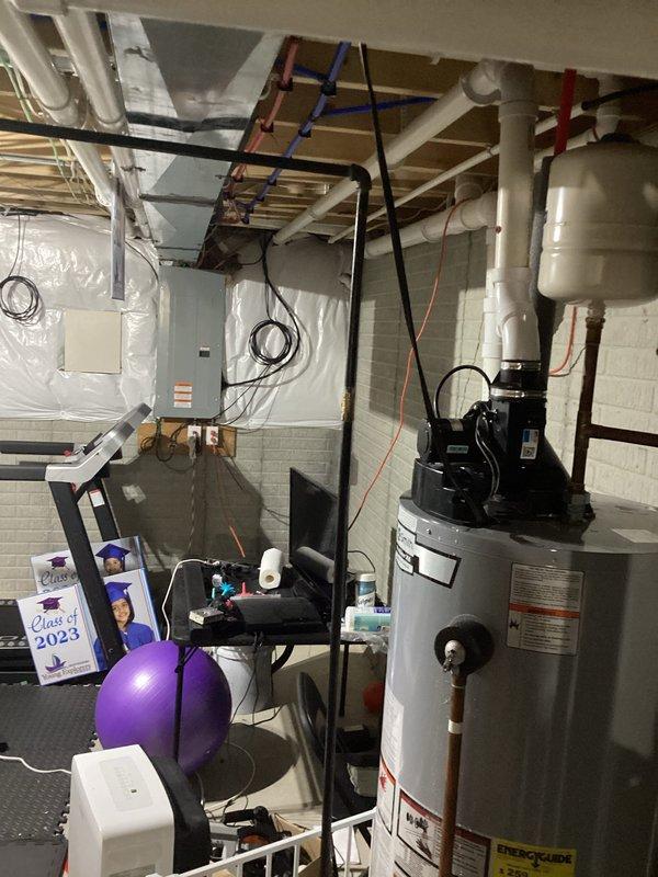 Responded to emergency service call for water heater leaking onto basement floor. Upon arrival, conducted thorough inspection of A.O. Smith tanked water heater system and associated plumbing connections. Identified source of leak, assessed condition of unit, pressure tank, and circulation pump assembly mounted on top of water heater. Documented existing installation including PVC supply and drainage lines, shut-off valves with red and blue handles, and overall mechanical system configuration for service records.