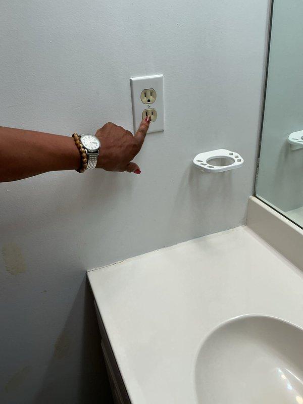 Provided estimate for electrical repairs including installation of one exterior GFCI outlet, replacement of non-GFCI bathroom outlet with code-compliant GFCI protection, and repair of loose living room receptacle. Inspected existing bathroom outlet on light blue wall near vanity sink and assessed weathered exterior outlet box with corroded turquoise cover on white vinyl siding showing signs of moisture exposure and age-related deterioration. Documented current conditions of electrical fixtures requiring upgrade to meet safety standards and resolve connection issues.