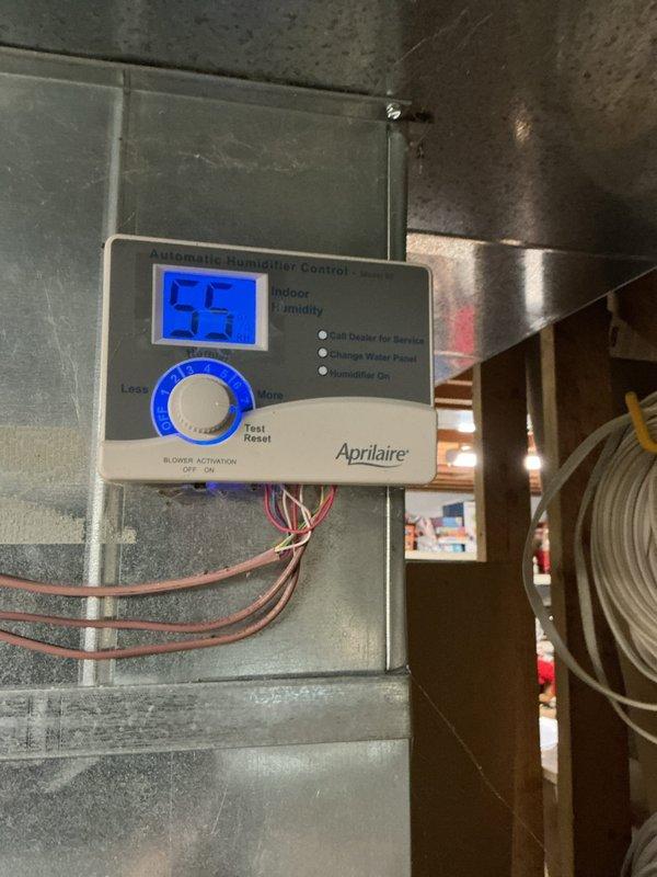 Responded to service call for non-functioning Aprilaire whole-home humidifier with reported lack of water flow and dry filter media. Upon inspection, verified humidifier control unit was set to 55% relative humidity but system was not delivering moisture to ductwork. Examined humidifier installation including water supply lines, filter pad condition, and control wiring connections. Documented current system configuration with digital humidifier controller mounted on supply ductwork and filter assembly installed in overhead plenum. Assessed copper water supply tubing routing and electrical connections to ensure proper installation standards were maintained.