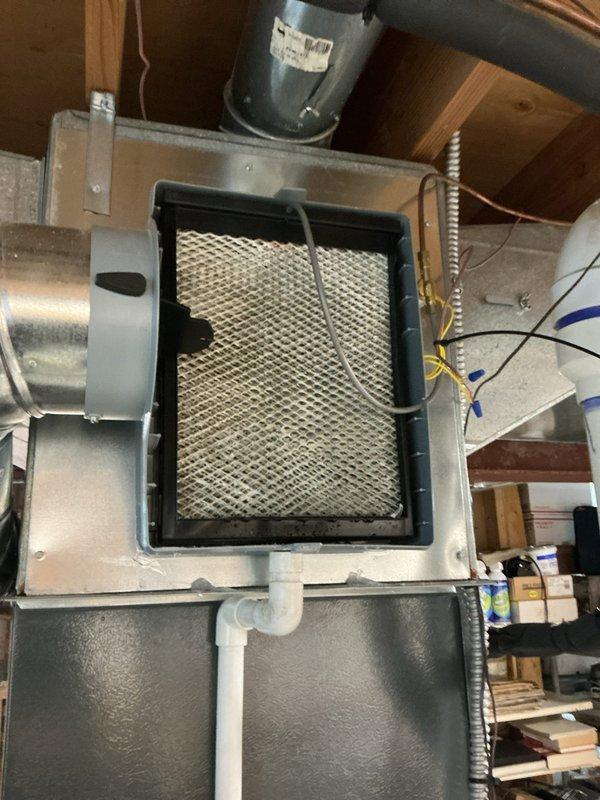 Responded to service call for non-functioning Aprilaire whole-home humidifier with reported lack of water flow and dry filter media. Upon inspection, verified humidifier control unit was set to 55% relative humidity but system was not delivering moisture to ductwork. Examined humidifier installation including water supply lines, filter pad condition, and control wiring connections. Documented current system configuration with digital humidifier controller mounted on supply ductwork and filter assembly installed in overhead plenum. Assessed copper water supply tubing routing and electrical connections to ensure proper installation standards were maintained.
