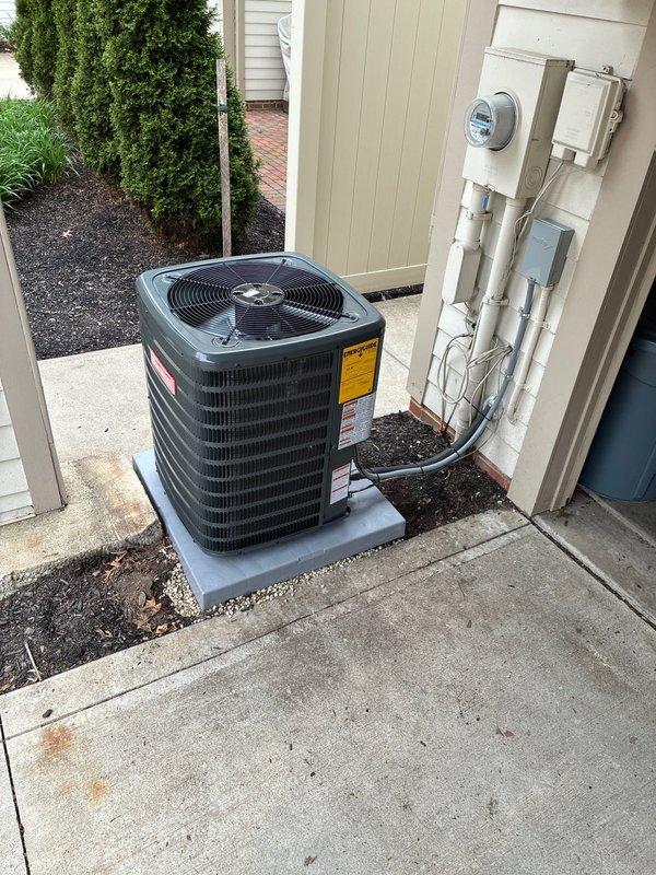 Completed full air conditioning system installation at residential property. Installed new black condenser unit on concrete pad with proper clearance from structure, ensuring adequate airflow around unit. Mounted and wired smart thermostat control system (Dragonfly Internet Thermostat) with dual circuit board configuration inside clear protective enclosure on interior wall. Routed and connected refrigerant lines and electrical wiring through PVC conduit along exterior wall, integrating with existing electrical meter infrastructure. Verified all electrical connections, tested system operation, and confirmed proper communication between thermostat and outdoor unit. System startup successful with all components functioning as designed.