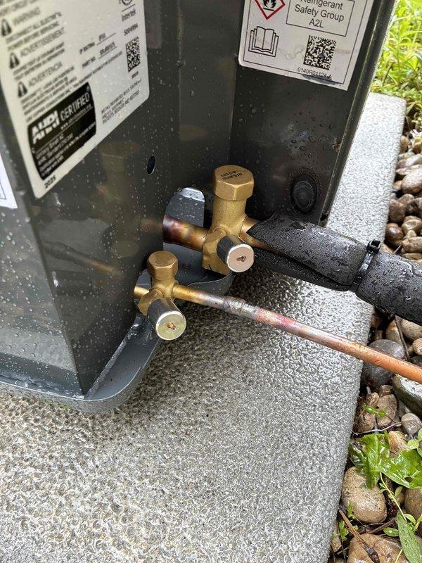 Completed full HVAC system installation including new outdoor condensing unit and indoor evaporator coil. Installed gray A2L-rated air conditioning condenser on existing concrete pad in residential backyard with proper clearances from structure and property line. Ran electrical conduit along exterior wall to power unit per code requirements. Connected refrigerant lines using brass service valves and properly insulated copper line set to prevent condensation. System charged with R32 refrigerant per manufacturer specifications. Verified all electrical connections secure, tested system operation, and confirmed proper airflow and cooling performance. Installation includes updated A2L safety-compliant equipment with appropriate labeling and documentation.