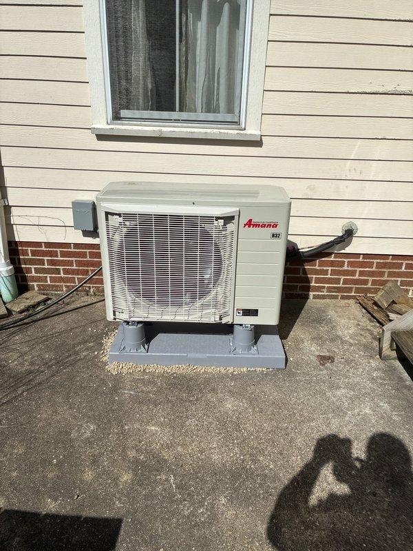 Completed heat pump installation with Amana outdoor unit mounted on platform against building exterior. Installed FLNR 20A Littelfuse fuses in electrical disconnect, established refrigerant line sets and electrical conduit connections from outdoor unit to building, and verified all electrical components properly secured and operational.