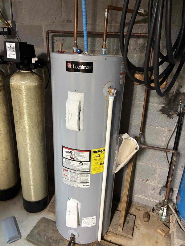 Responded to service call for reported water heater leak with undetermined location. Upon arrival, performed comprehensive visual inspection of Lochinvar tanked water heater unit and surrounding plumbing connections. Examined all accessible areas including tank body, top connections, copper supply lines, blue flexible conduit, relief valve, drain valve, and base of unit. Inspected floor area for active water pooling or moisture patterns. Checked connections to adjacent water treatment equipment including softener tanks and pressure tank. Documented equipment condition and installation configuration with photographs for service records.