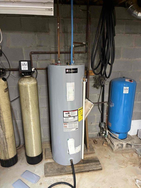 Responded to service call for reported water heater leak with undetermined location. Upon arrival, performed comprehensive visual inspection of Lochinvar tanked water heater unit and surrounding plumbing connections. Examined all accessible areas including tank body, top connections, copper supply lines, blue flexible conduit, relief valve, drain valve, and base of unit. Inspected floor area for active water pooling or moisture patterns. Checked connections to adjacent water treatment equipment including softener tanks and pressure tank. Documented equipment condition and installation configuration with photographs for service records.