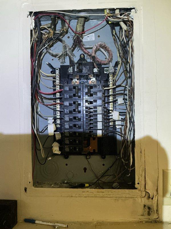 Conducted electrical inspection for reported porch light malfunction. Documented electrical panel configuration showing two rows of circuit breakers with multiple wire connections entering from top and sides, noting disorganized wiring throughout panel cavity. Also photographed basement mechanical systems including circulation pump and associated plumbing infrastructure for comprehensive site assessment.