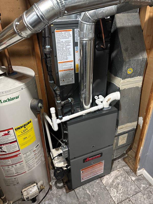 Completed installation of new Amana HVAC furnace system in residential utility room. Unit was properly positioned, secured, and connected with all necessary ductwork, including silver metallic supply ducting and proper venting configurations. Installed white PVC condensate drainage piping with appropriate fittings and elbows to ensure proper system drainage. All electrical connections were completed to manufacturer specifications, and safety labels were affixed to equipment per code requirements. System was tested and verified operational upon completion.