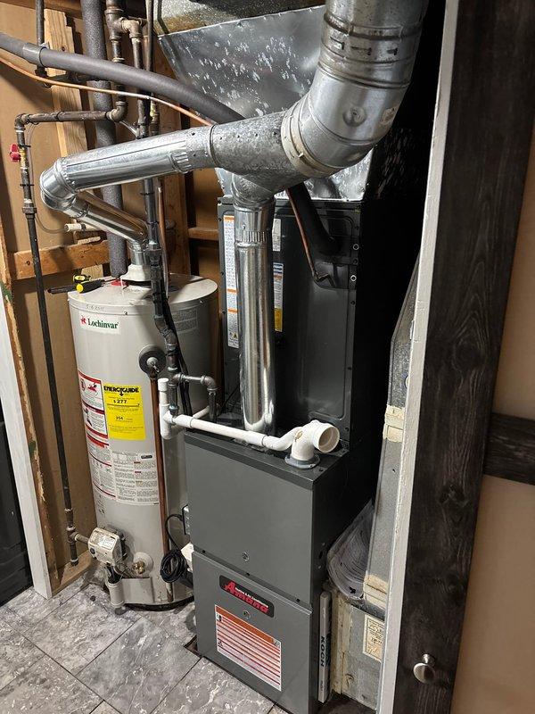 Completed installation of new Amana HVAC furnace system in residential utility room. Unit was properly positioned, secured, and connected with all necessary ductwork, including silver metallic supply ducting and proper venting configurations. Installed white PVC condensate drainage piping with appropriate fittings and elbows to ensure proper system drainage. All electrical connections were completed to manufacturer specifications, and safety labels were affixed to equipment per code requirements. System was tested and verified operational upon completion.