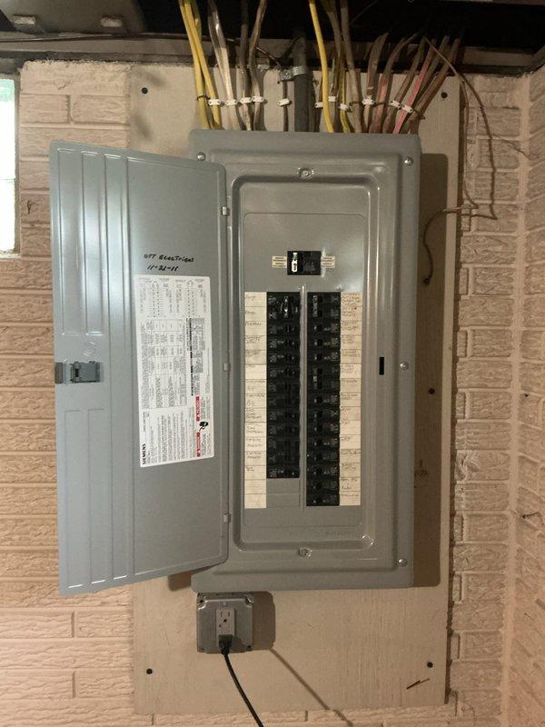 Completed electrical estimate for exterior outlet installation. Assessed existing electrical panel with dual rows of circuit breakers and evaluated wire routing from interior panel through wall to proposed exterior outlet location. Identified penetration point in exterior siding where new weatherproof outlet box will be mounted and documented current conditions including exposed opening and existing utility access panels on deck area.