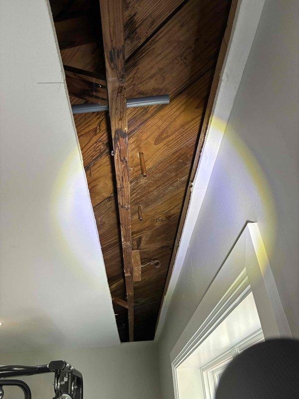 Returned to property for copper piping installation following burst pipe repair. Previous visit in January identified the need for wall removal to access affected areas. Upon arrival, confirmed that drywall had been removed as requested, exposing ceiling joists and structural framing. Documented exposed wooden beams, rafters, and parallel joists in preparation area. Verified access points were adequate for copper pipe replacement work. Photographed ceiling cavity showing weathered structural elements and newly accessible areas where piping installation will occur. Work area is now properly prepared for the copper piping installation to proceed.