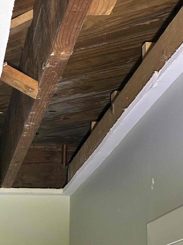 Returned to property for copper piping installation following burst pipe repair. Previous visit in January identified the need for wall removal to access affected areas. Upon arrival, confirmed that drywall had been removed as requested, exposing ceiling joists and structural framing. Documented exposed wooden beams, rafters, and parallel joists in preparation area. Verified access points were adequate for copper pipe replacement work. Photographed ceiling cavity showing weathered structural elements and newly accessible areas where piping installation will occur. Work area is now properly prepared for the copper piping installation to proceed.