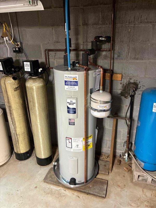 Completed installation of 50-gallon residential water heater with thermal expansion tank and drain pan in basement utility area. Unit was properly connected to existing copper supply lines, with expansion tank mounted adjacent to water heater to accommodate thermal expansion and protect against pressure buildup in closed plumbing systems. All connections were secured per manufacturer specifications and local plumbing codes.