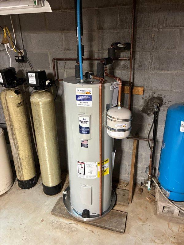 Completed installation of 50-gallon residential water heater with thermal expansion tank and drain pan in basement utility area. Unit was properly connected to existing copper supply lines, with expansion tank mounted adjacent to water heater to accommodate thermal expansion and protect against pressure buildup in closed plumbing systems. All connections were secured per manufacturer specifications and local plumbing codes.