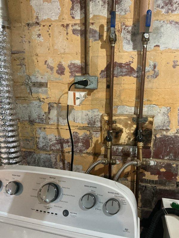 Completed comprehensive electrical inspection of residential basement utility area. Documented existing electrical infrastructure including exposed wiring in unfinished ceiling joists, junction boxes mounted to copper plumbing lines, and electrical outlets servicing utility equipment. Photographed conditions of electrical components in laundry area showing transformer/adapter installation, visible cable routing along wooden beams, and various electrical connections throughout the space. Inspection revealed aging infrastructure with multiple systems present including yellow electrical cable runs, flexible metal conduit, and blue junction box installations. All findings documented photographically for record purposes and future reference.