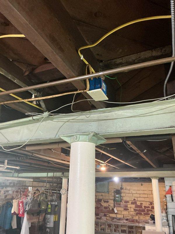 Completed comprehensive electrical inspection of residential basement utility area. Documented existing electrical infrastructure including exposed wiring in unfinished ceiling joists, junction boxes mounted to copper plumbing lines, and electrical outlets servicing utility equipment. Photographed conditions of electrical components in laundry area showing transformer/adapter installation, visible cable routing along wooden beams, and various electrical connections throughout the space. Inspection revealed aging infrastructure with multiple systems present including yellow electrical cable runs, flexible metal conduit, and blue junction box installations. All findings documented photographically for record purposes and future reference.