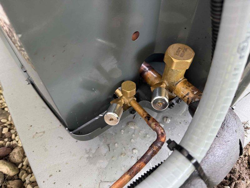 Completed installation of new air conditioning system with heat exchanger assembly and refrigerant line connections. Installed four-tube copper heat exchanger unit within metal housing frame, connected main refrigerant lines, and established all necessary valve connections at the base unit with proper fittings to ensure system integrity and optimal cooling performance.
