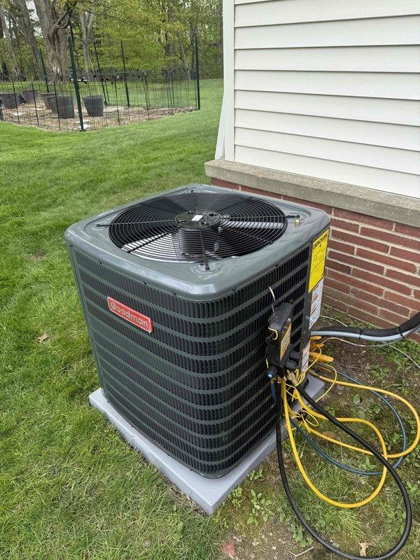 Completed installation of new Goodman air conditioning system on existing concrete pad adjacent to residential structure. Unit positioned on level concrete base with proper clearances from brick foundation and vinyl siding exterior. Performed electrical connections, refrigerant line installation, and system startup procedures. Conducted diagnostic testing using electronic testing equipment to verify proper amperage draw, voltage levels, and refrigerant pressures. System commissioned and operating within manufacturer specifications.