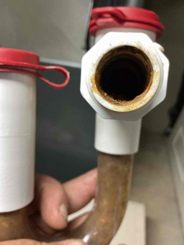 Replaced deteriorated condensate drain line showing heavy mineral buildup and corrosion. Removed old PVC drain assembly with significant scale deposits restricting water flow, installed new drain piping and fittings, and performed complete system flush to ensure proper drainage and prevent future clogs.