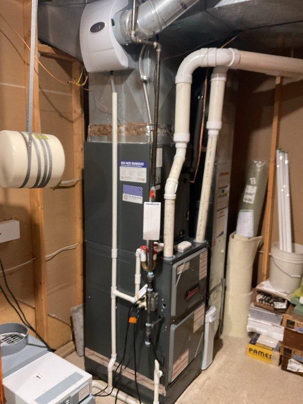 # HVAC Maintenance - Cooling System Service

Completed comprehensive preventive maintenance on residential cooling system during early afternoon service call. Performed thorough inspection of indoor furnace unit and associated HVAC components in basement mechanical room, verifying proper operation of all safety labels and manufacturer specifications. Examined PVC drainage and ventilation piping system, confirmed red valve handles operational and condensate drain lines clear of obstructions.

Inspected metallic ductwork connections and white ventilation components for secure mounting and proper airflow configuration. Verified all wiring and electrical connections along wooden framing were secure and up to code.

Proceeded to outdoor disconnect panel to service air conditioning electrical components. Inspected and tested cylindrical capacitor for proper microfarad rating and functionality. Examined electrical contactor relay, verified all terminal connections secure with proper wire rout