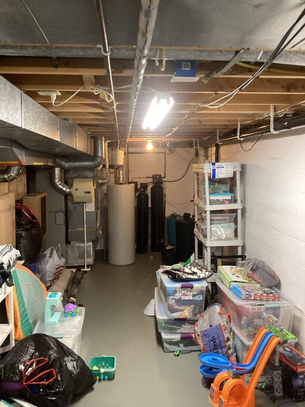 Completed plumbing inspection of basement utility area to assess gas line installation requirements. Documented existing mechanical systems, including furnace, water heater, water treatment equipment, and current pipe routing through ceiling joists to determine optimal path and materials needed for new gas line installation.