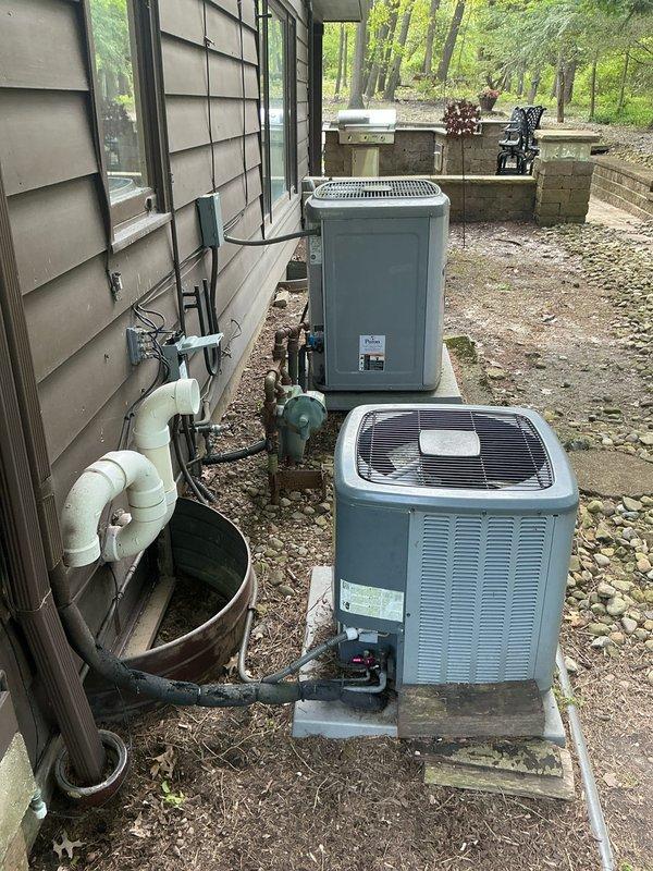 Completed HVAC system replacement estimate for attic installation with customer-provided ladder access. Documented existing electrical panel configuration with exposed circuit breakers and junction box connections, along with current outdoor unit placement featuring dual air conditioning units on concrete pads with PVC drainage system and refrigerant line routing. Photographed complete system layout including electrical infrastructure and exterior equipment positioning to provide comprehensive replacement specifications.