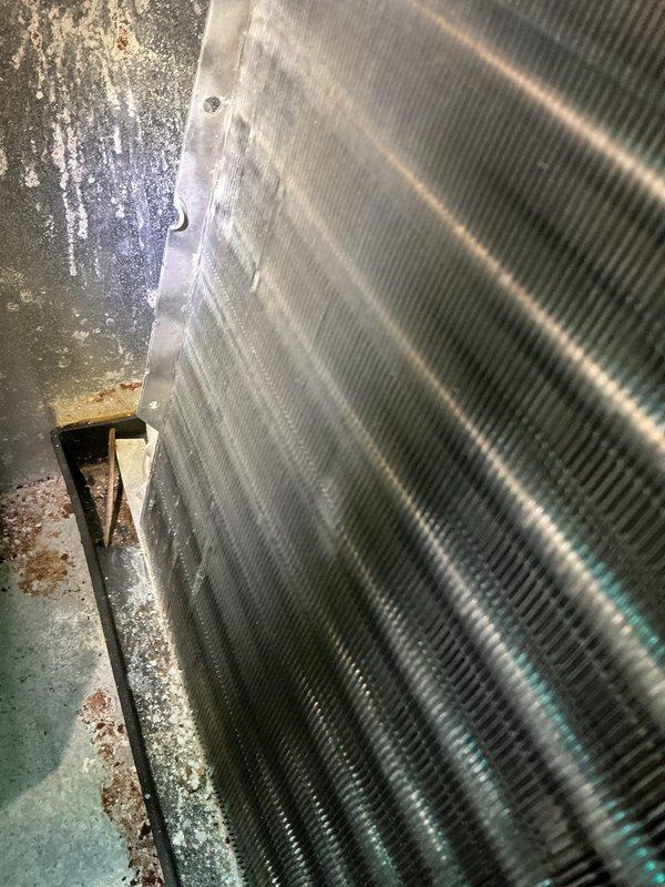 Completed scheduled cooling system maintenance on attic-mounted air handler unit. Accessed evaporator coil assembly through front service panel and performed thorough inspection of coil fins and heat exchanger surfaces. Coil fins showed relatively clean condition with minimal debris accumulation. Noted evidence of previous moisture exposure and minor oxidation on metal framework and base components, though coil integrity remains intact. Unit operational and functioning within normal parameters following maintenance completion.