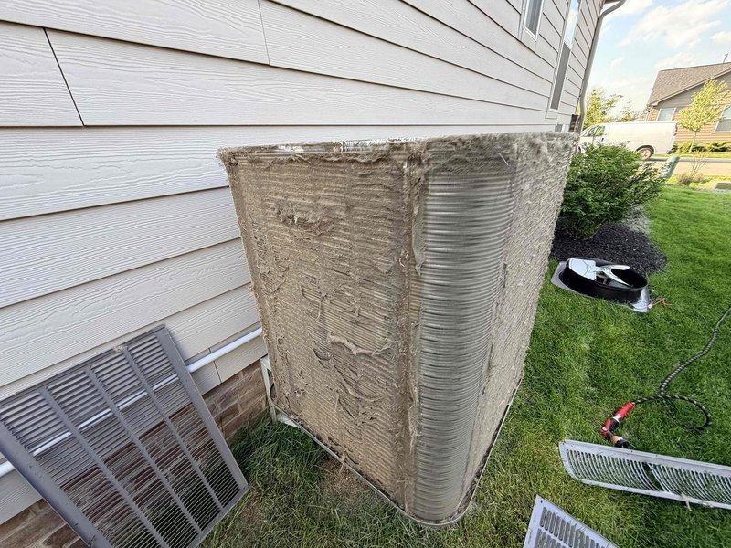 Performed comprehensive cooling system maintenance on outdoor condensing unit. Unit exhibited heavy accumulation of dust, dirt, and debris on exterior surfaces, top panel, and condenser coil fins. Removed access panels and cleaned condenser coils using backpack blower to remove loose debris and particulate matter from aluminum fins and ventilation grilles. Reassembled unit components and verified proper airflow through cleaned coil surfaces to restore optimal heat transfer efficiency.