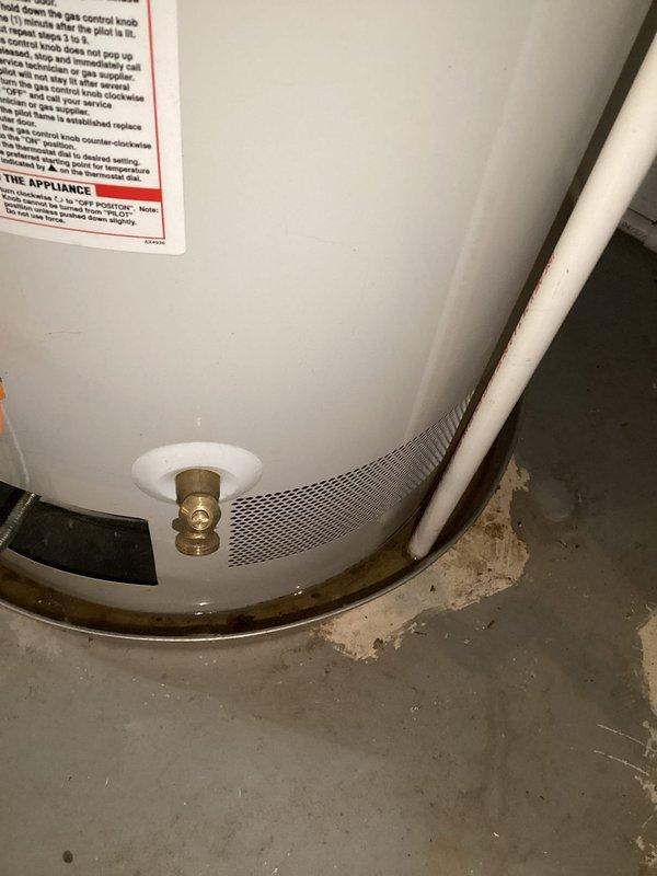 Responded to residential water heater leak. Upon arrival, inspected tanked water heater unit and identified active leak at base with visible water accumulation on concrete floor and corrosion staining around lower fittings. Assessed brass drain valve and bottom connections showing signs of deterioration and moisture intrusion. Drip pan exhibited rust discoloration indicating prolonged exposure to leaking water. Documented condition with photographs showing extent of water damage and compromised seals at tank base. Recommended replacement of unit due to tank integrity failure and advised customer of leak source and necessary corrective action.